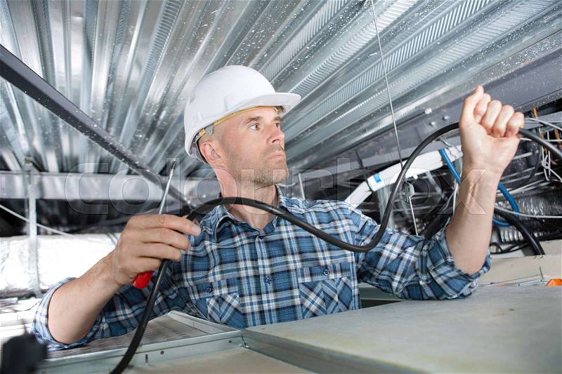 Electrician installing cables in roof, stock photo