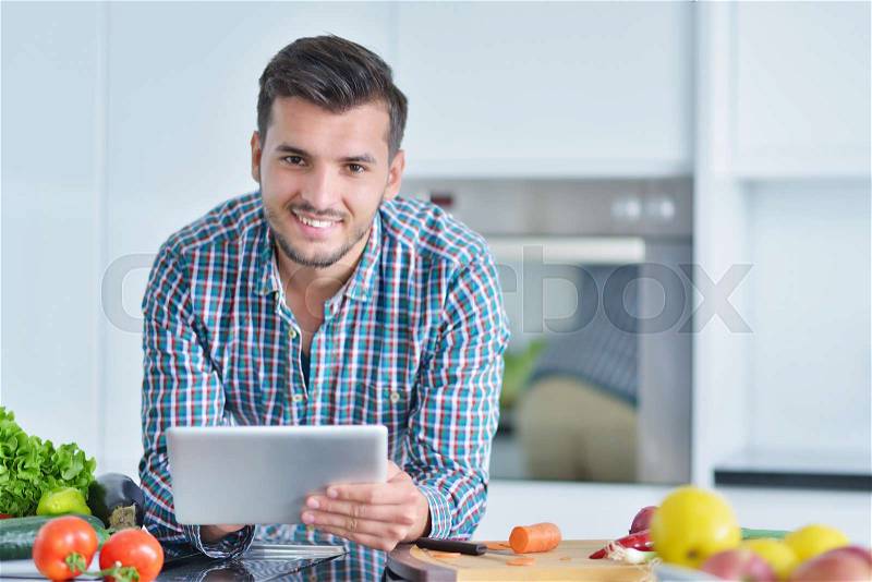 Happy man using digital tablet in kitchen at home, stock photo