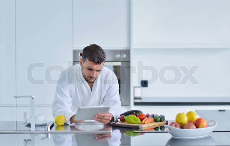 Young man in bathrobe sitting on kitchen worktop and having a cup of tea, stock photo