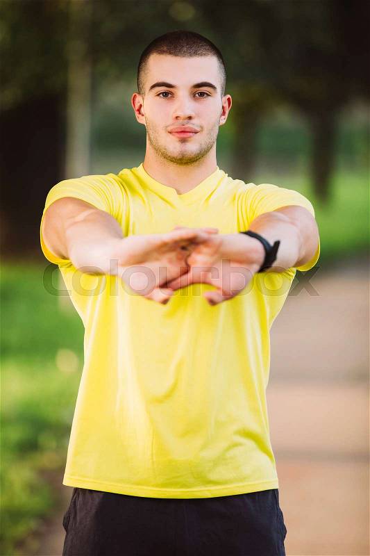 Fitness man stretching arm shoulder before outdoor workout. Sporty male athlete in an urban park warming up, stock photo