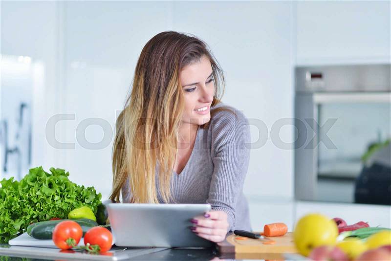 Young woman is making online shopping by tablet computer. Housewife found new recipe for cooking in a kitchen, stock photo
