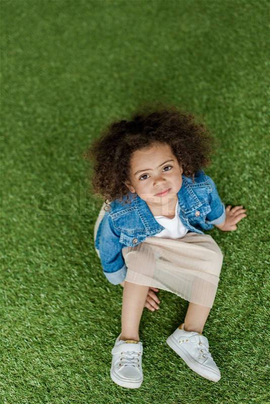 Cute african american curly girl resting on lawn, stock photo