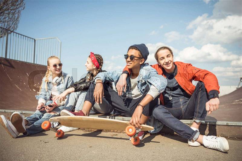 Happy teenagers group sitting together and talking at skateboard park, stock photo