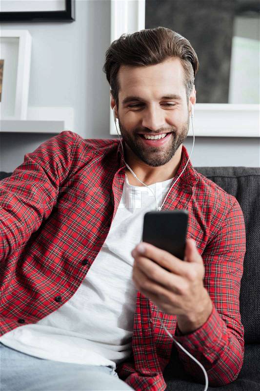 Young bearded man in earphones using smartphone to make a videocall, stock photo