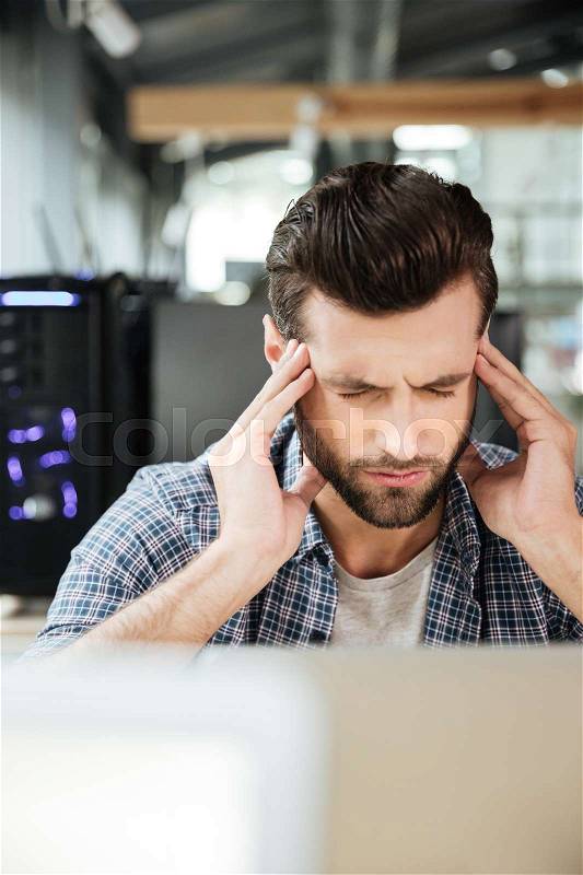 Image of young concentrated thinking man in office coworking while using laptop computer, stock photo