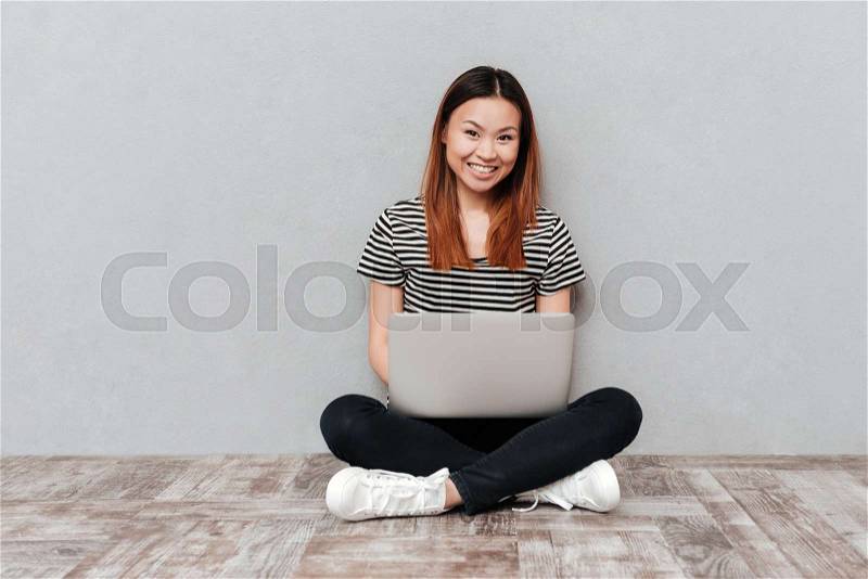 Positive cheerful woman looking camera while sitting on floor with laptop isolated, stock photo