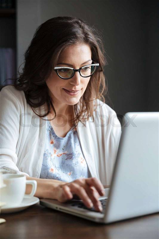 Portrait of a smiling mature woman working on laptop at the table indoors, stock photo