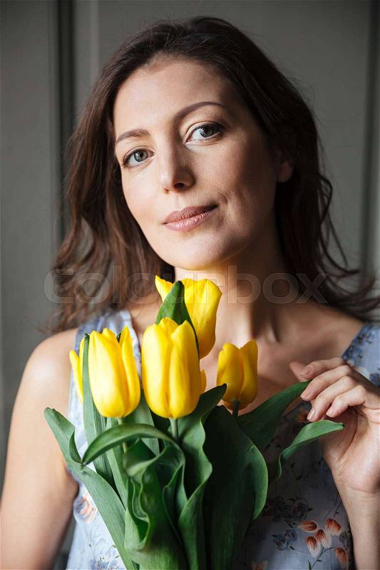 Image of happy woman writer sitting indoors while holding tulips. Looking at camera, stock photo