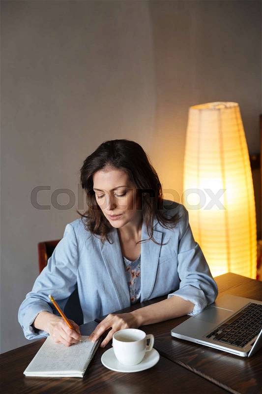 Picture of thinking woman writer sitting indoors using laptop computer. Looking at notebook, stock photo