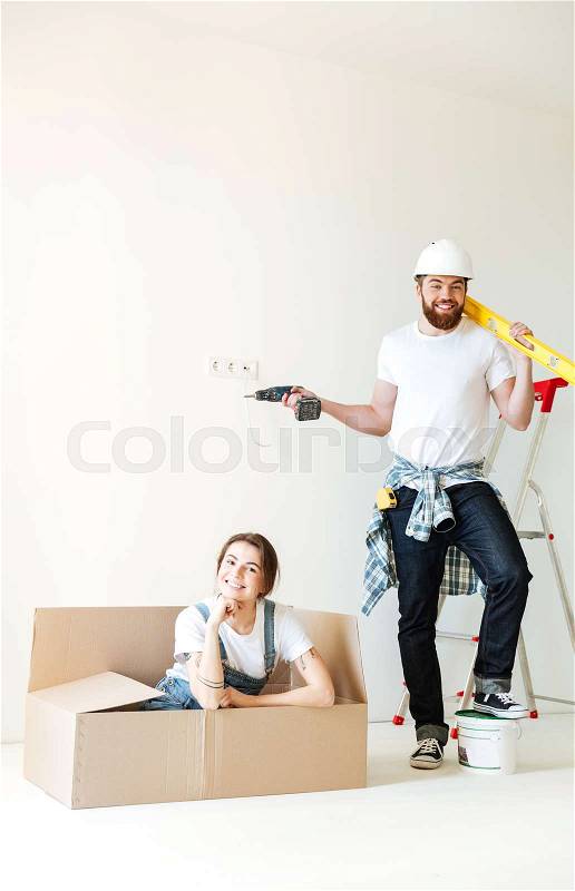Young man with tools posing while his woman sitting in box and smiling isolated, stock photo