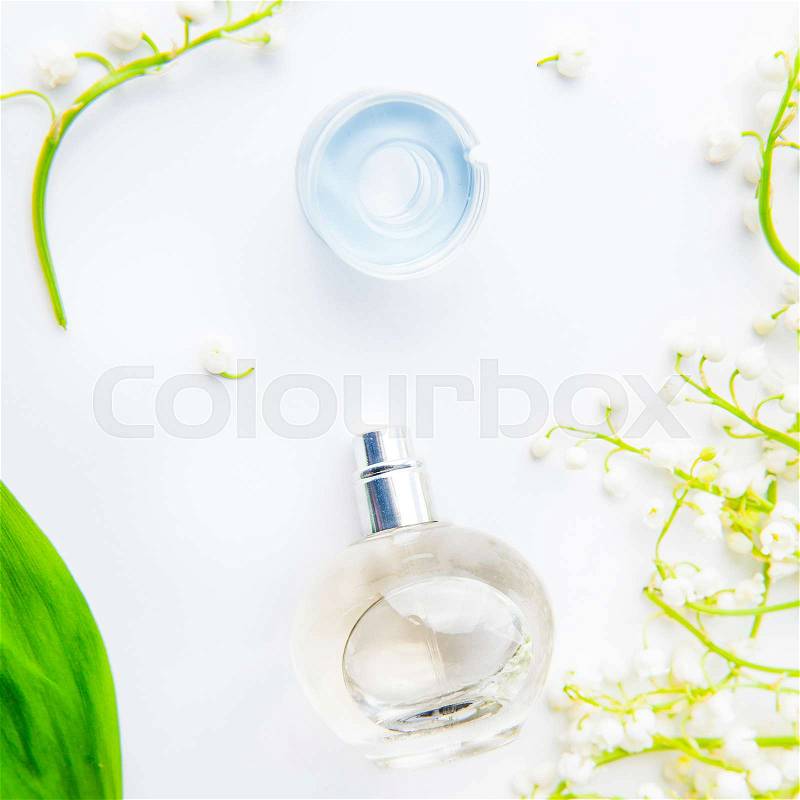 Square Beauty concept card. Flat lay with Orbicular perfume bottle surrounded by fresh lilies of the valley, may-lily flowers and green leaf on the white background. Top view. Selective focus, stock photo
