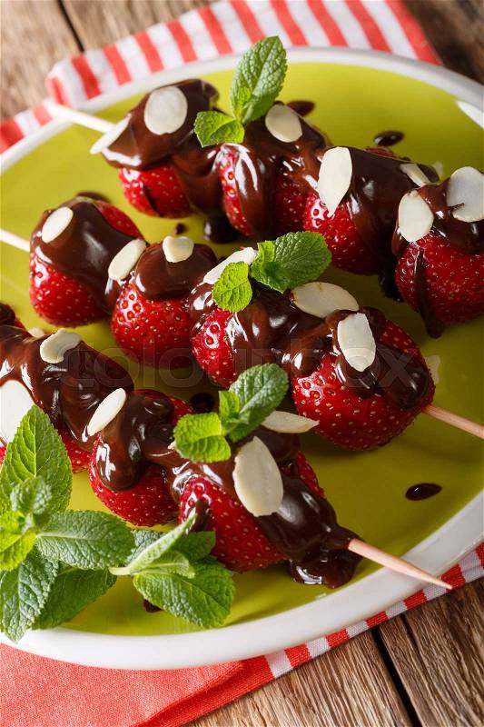 Skewers with fresh strawberries are decorated with chocolate, mint and almonds on a plate. vertical , stock photo