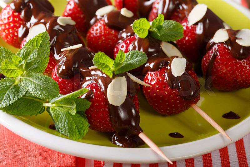 Skewers with strawberries decorated with chocolate, mint and almonds close-up on a plate. horizontal , stock photo