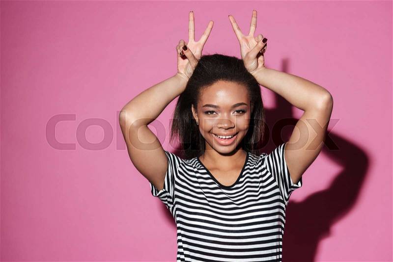 Portrait of a smiling happy african girl showing peace sign with two hands isolated over pink background, stock photo