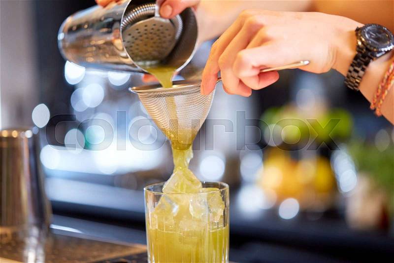 Alcohol drinks, people and luxury concept - close up of woman bartender hands pouring cocktail from shaker to glass at bar, stock photo