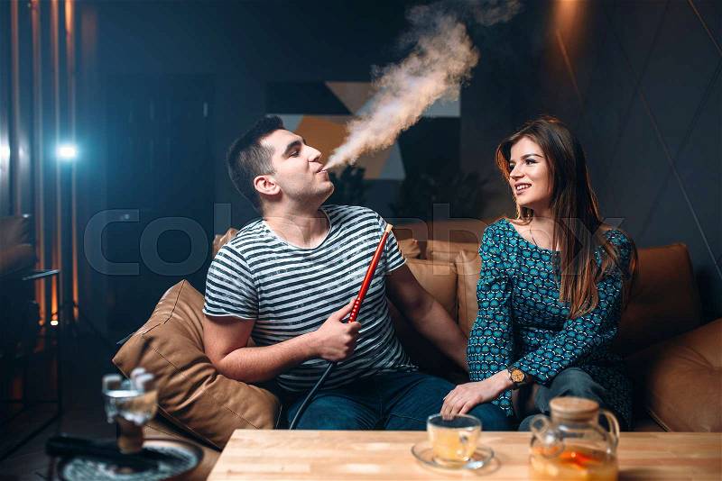 Young couple smoking hookah on leather couch at the bar, tobacco smoke and relaxation, stock photo