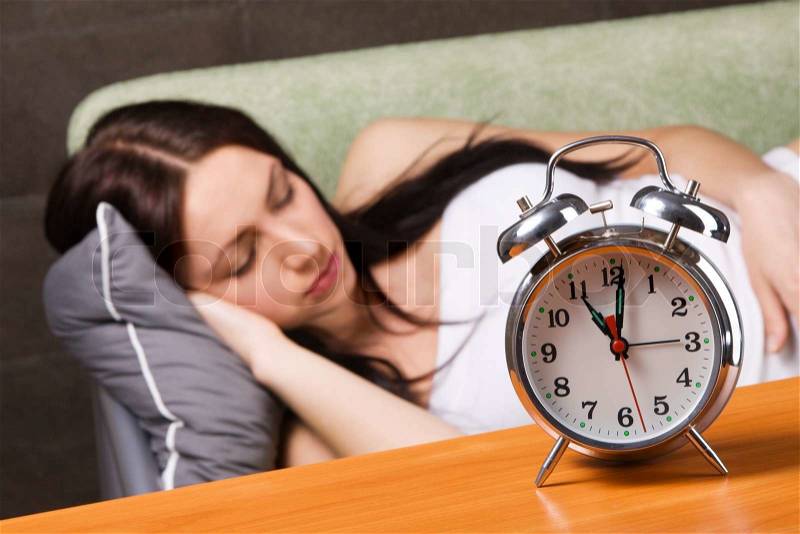 Vintage alarm clock, with beautiful young woman sleeping in the background, stock photo