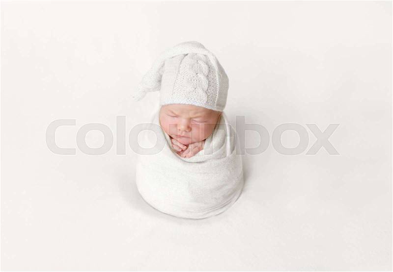 Lovely baby sleeping wrapped up with a blanket into a sitting position, white hat, stock photo