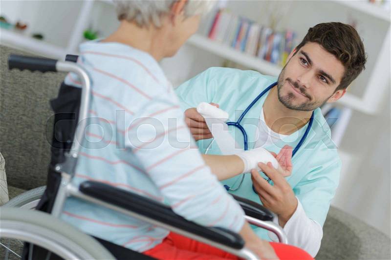 Young male nurse bandaging elderly woman\'s wrist, stock photo