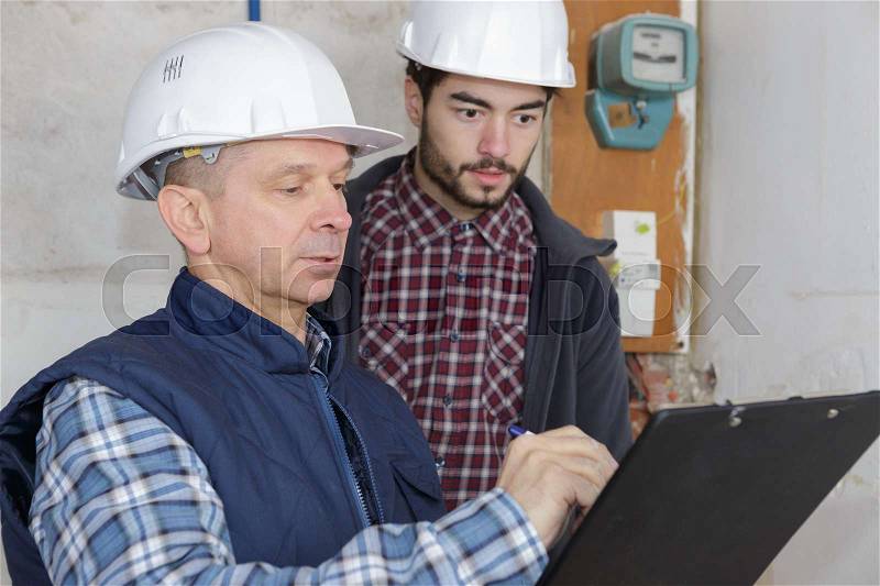 Builders with clipboard and electrical panel indoors, stock photo