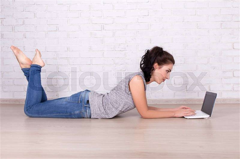Side view of young beautiful woman lying on the floor with laptop, stock photo