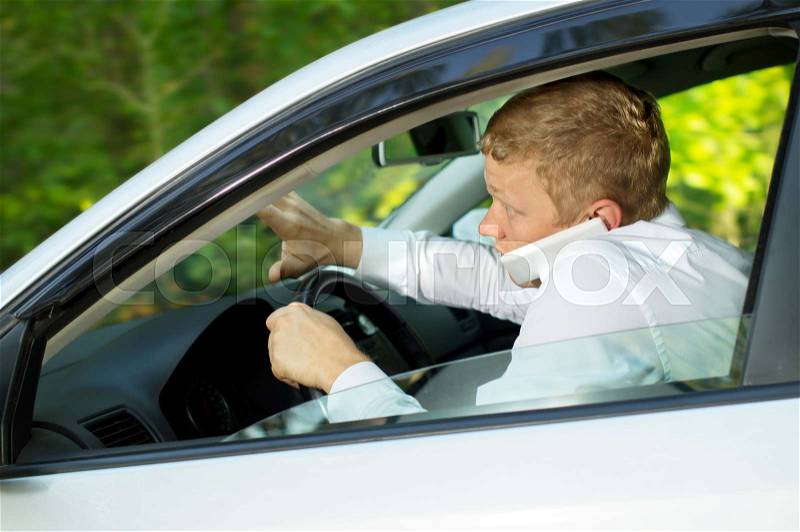Young man uses the phone behind the wheel of a car, creating an emergency situation, stock photo