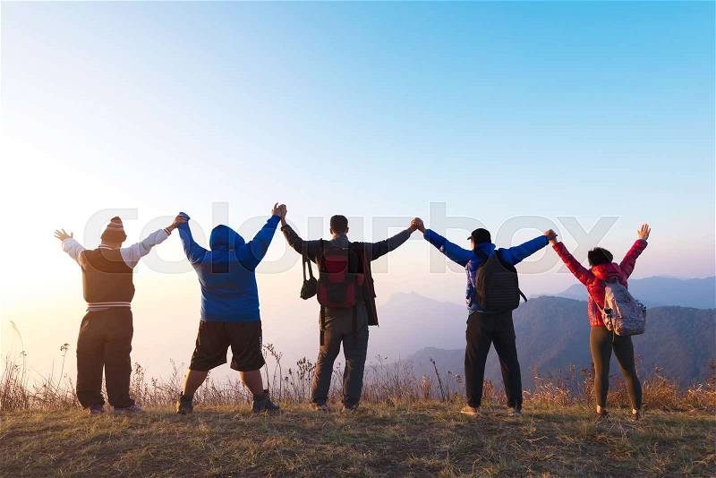Group of four people stands on the top of mountain in winner pose. Team or teamwork success concept.Space for text. Travel concept, stock photo