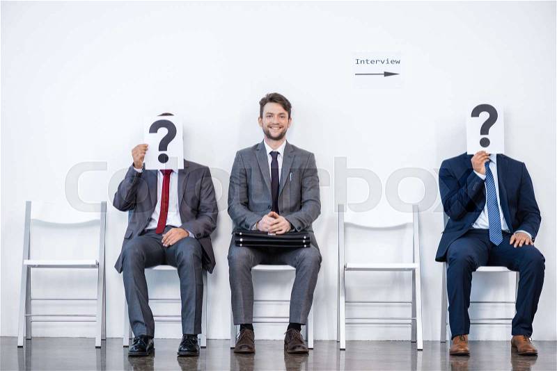 Businesspeople sitting in queue and waiting for interview, holding question marks in office, business concept, stock photo