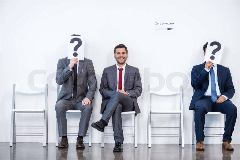 Businesspeople sitting in queue and waiting for interview, holding question marks in office, business concept, stock photo