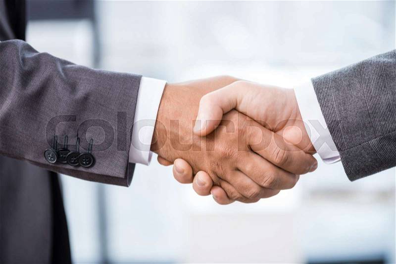 Close-up partial view of two businessmen in formal wear shaking hands, business concept, stock photo