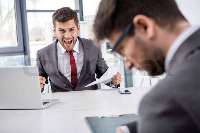 Angry boss with documents shouting at upset colleague at workplace, stock photo
