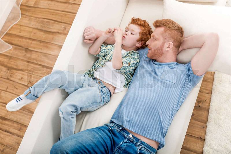 High angle view of happy father and son lying together on sofa at home, family fun at home concept, stock photo