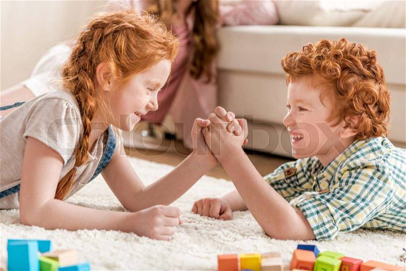 Side view of brother and sister playing arm wrestling, family fun at home concept, stock photo