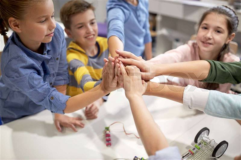 Education, children, technology, science and people concept - group of happy kids building robots and making high five gesture at robotics school, stock photo
