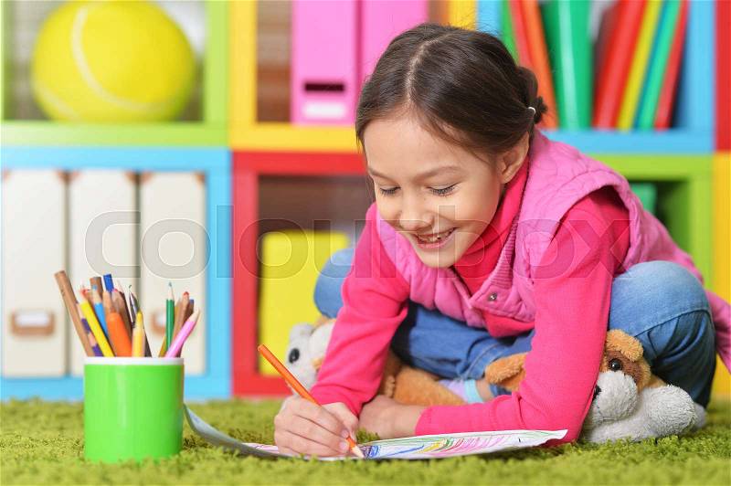 Cute little girl lying on floor and drawing picture, stock photo