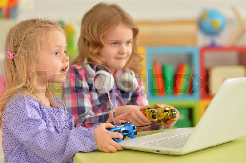 Two cute little sisters playing computer game with joysticks, stock photo