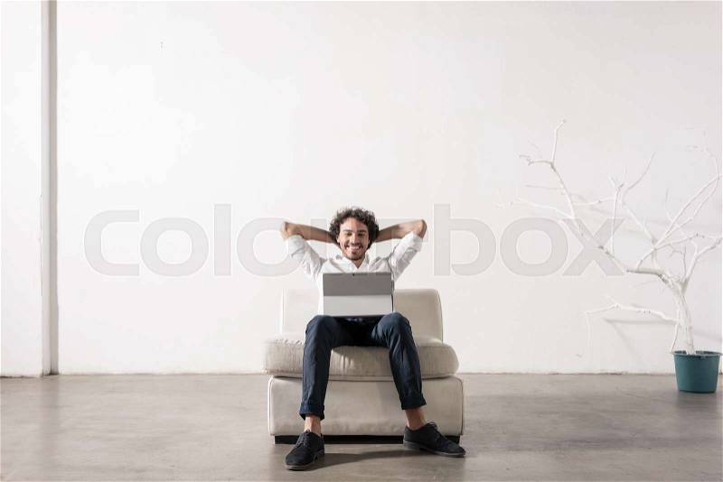 Ung man in agency sitting in armchair and working on laptop PC, stock photo