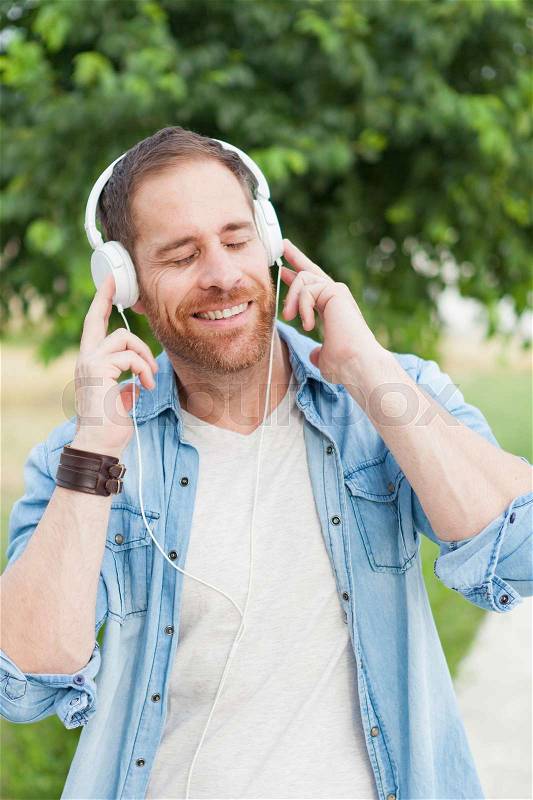 Casual guy with a denim clothes in a park listening music with his mobile, stock photo