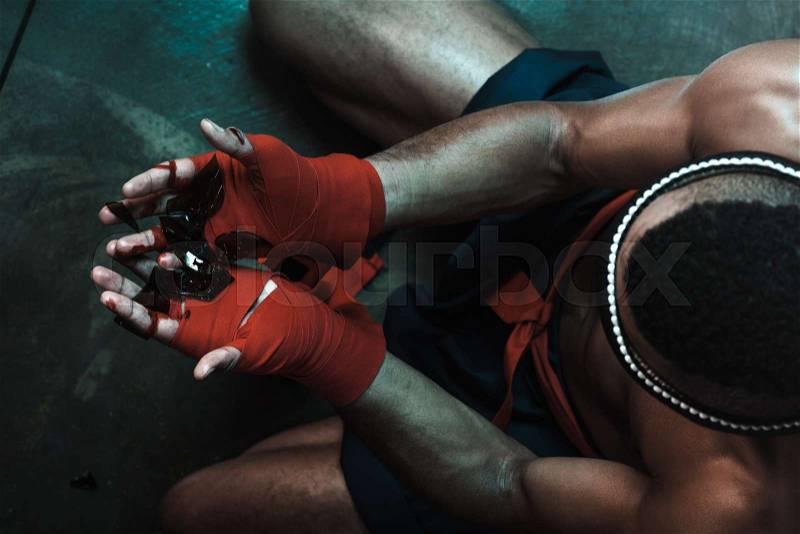 Muay Thai athlete holding glass shatters indoors, fight club concept, stock photo
