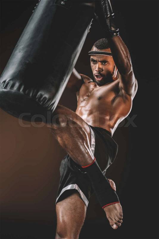 Concentrated muay thai fighter training with punching bag, action sport concept, stock photo