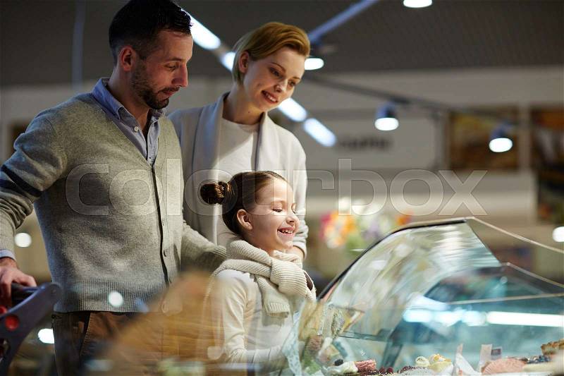 Portrait of happy family with cute little girl looking excited by pastry counter, choosing sweets for dessert and smiling, stock photo