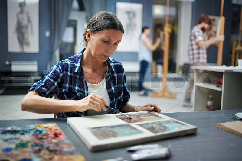 Portrait of mature student working in art studio painting pictures looking focused and concentrated, stock photo