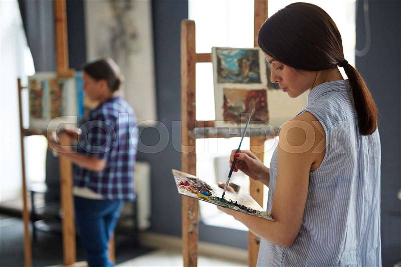 Back view portrait of young female student in art class, painting oil picture on canvas, stock photo