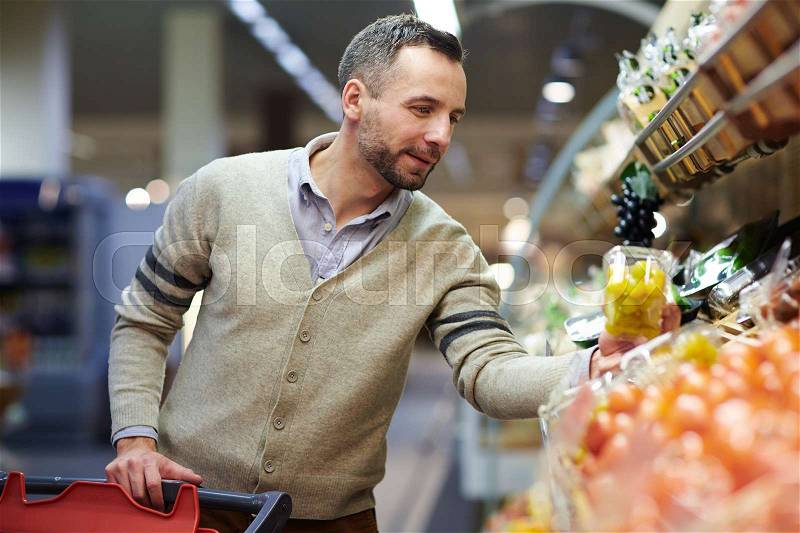 Portrait of smiling handsome man grocery shopping in supermarket, choosing food products from shelf, stock photo