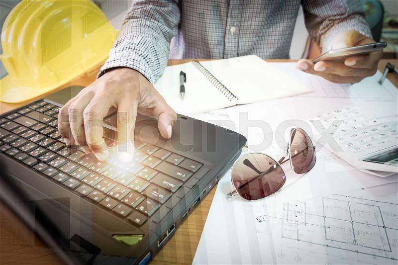 An architect working on illuminated laptop and mobile phone in office, stock photo