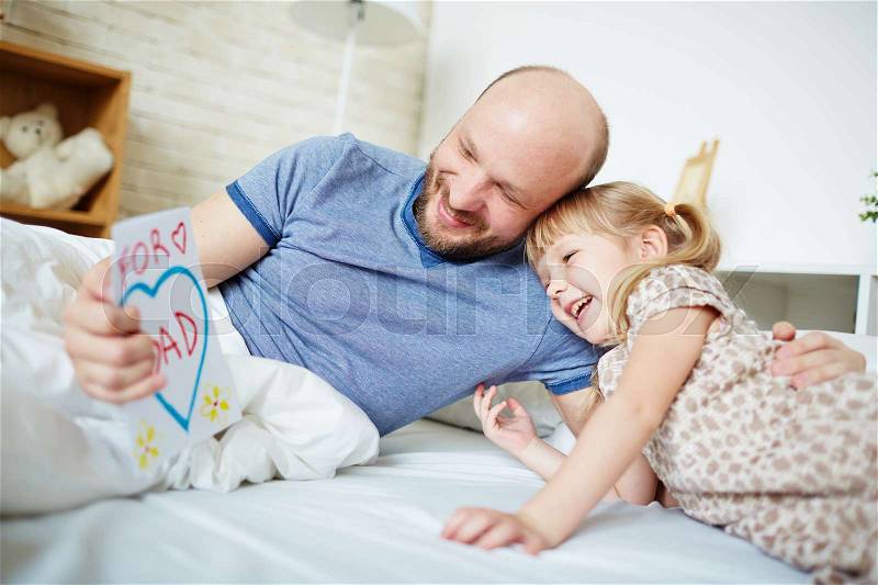 Happy man reading greetings for father day with little daughter near by, stock photo