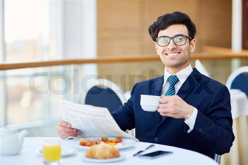Cheerful businessman with drink and newspaper sitting in cafe, stock photo