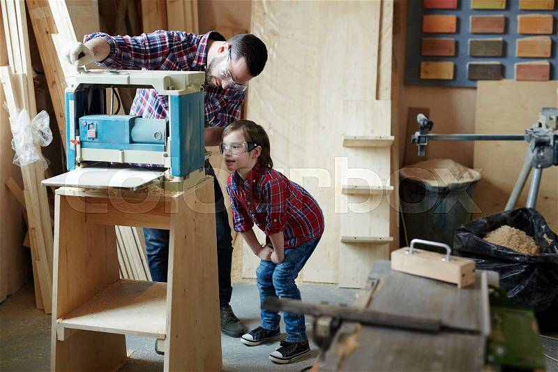 Young man showing his son how to work on planing machine, stock photo