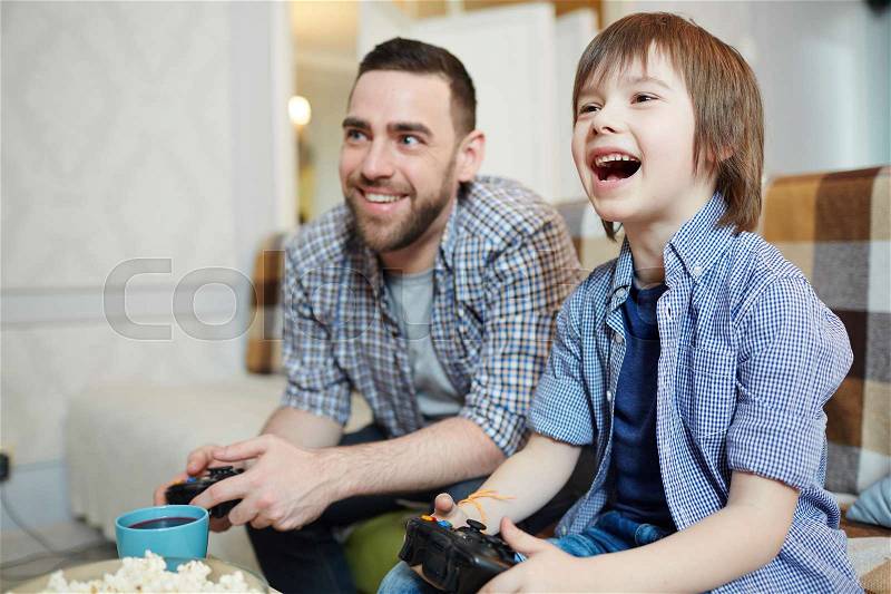 Excited boy with joystick gaming with father at home, stock photo