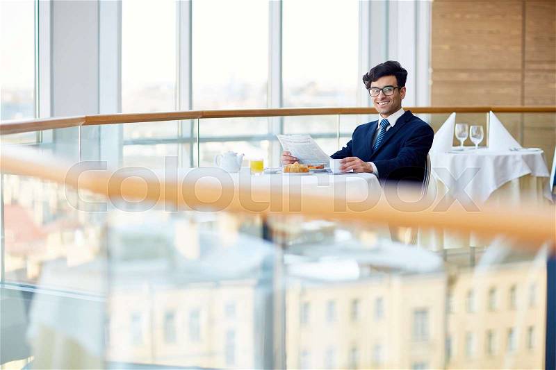 Successful young businessman with newspaper having breakfast in cafe, stock photo